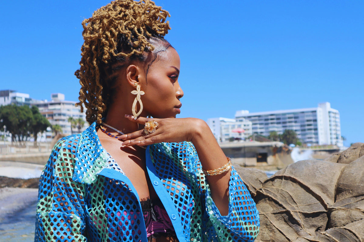 Woman with styled hair and blue top by a waterfront with stylish gold jewellery ireland dublin online at tamis jewellery